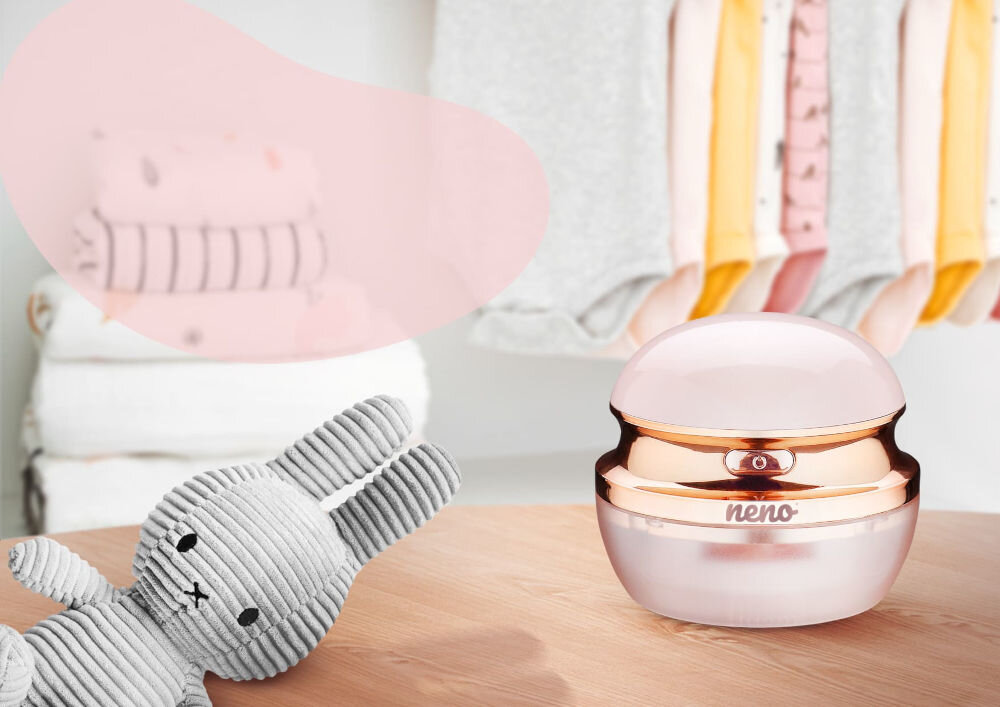 Golarka do ubrań NENO Merino Golarka do ubrań Neno postawiona na drewnianym blacie obok pluszowego królika, w tle wiszące ubranka dziecięce.