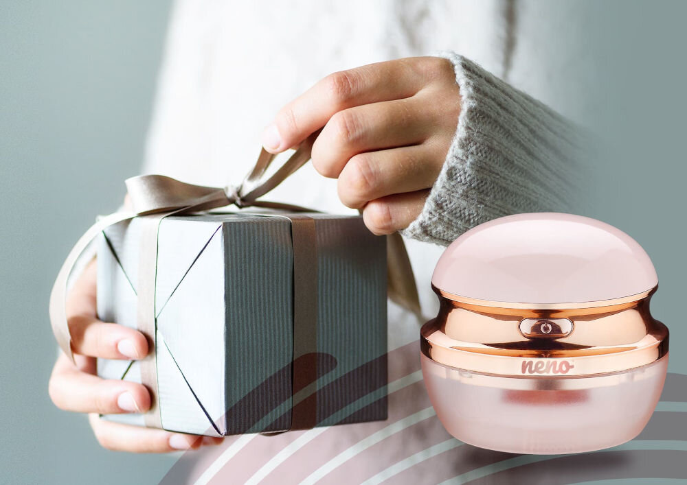 Golarka do ubrań NENO Merino Różowo-złota golarka do ubrań Neno obok dłoni trzymających zapakowany prezent z kokardą.