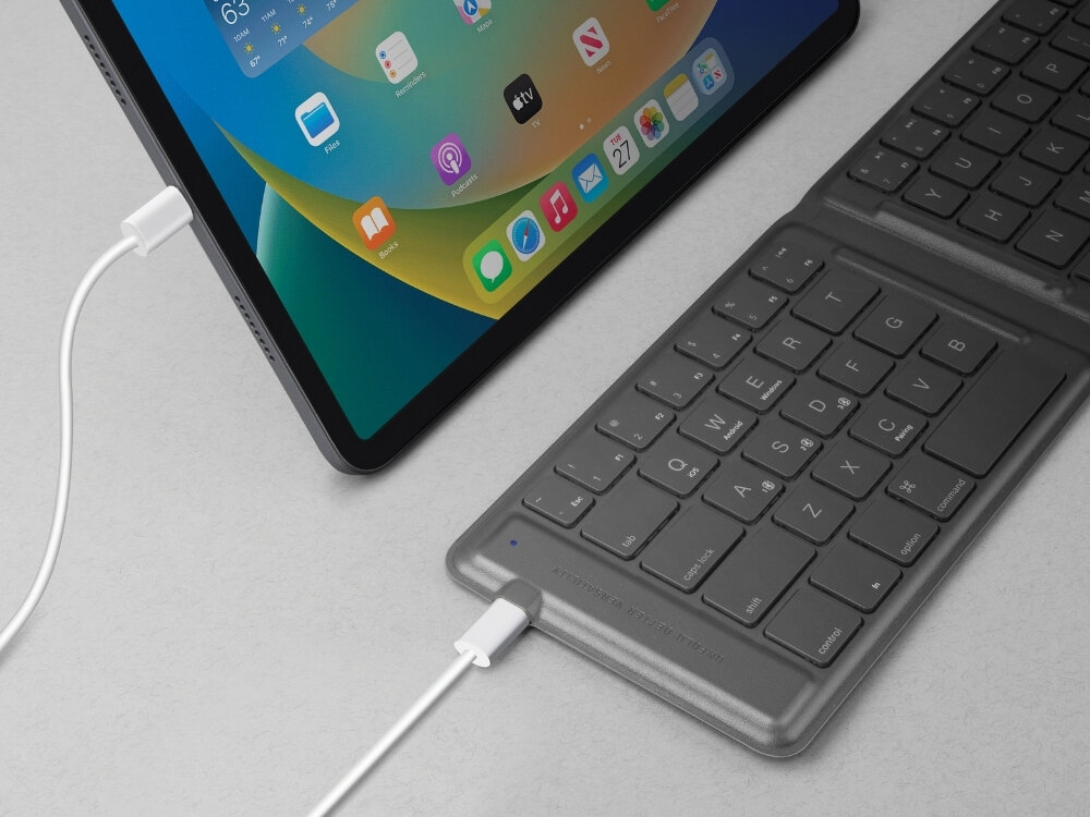 Na obrazie widać tablet z kolorowym ekranem oraz czarną klawiaturę podłączoną kablem. Klawiatura ma widoczne klawisze z literami i symbolami.