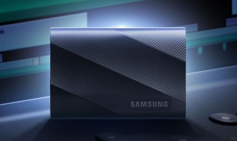 Na obrazie widoczny jest czarny dysk zewnętrzny z teksturą, z logo \'SAMSUNG\'. W tle znajdują się rozmyte elementy technologiczne.