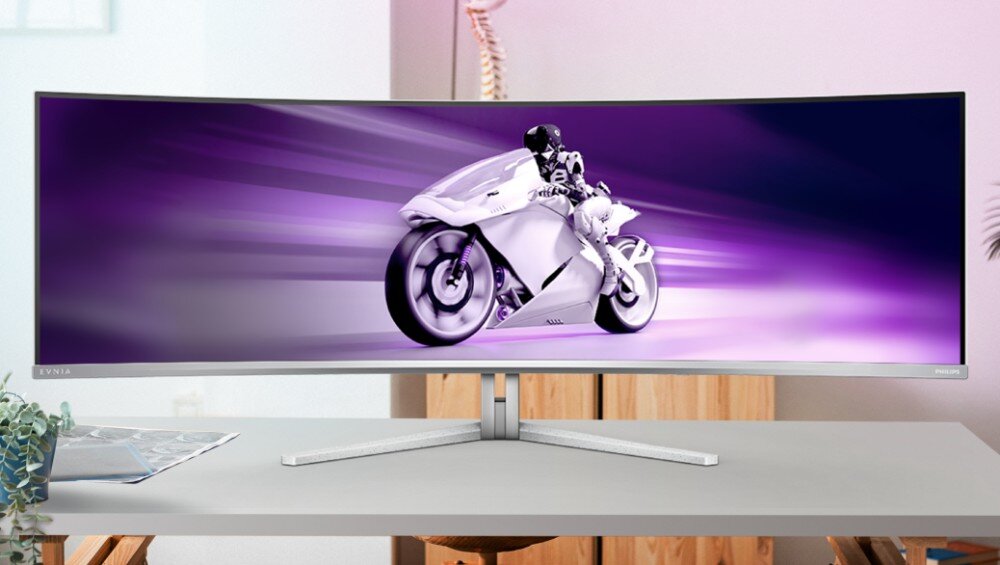 Monitor PHILIPS Evnia 49M2C8900 Zakrzywiony monitor panoramiczny stojący na biurku w jasnym pomieszczeniu, na ekranie grafika z motocyklistą jadącym na fioletowym tle z efektem rozmycia ruchu, zakrzywienie, przekątna, proporcje, rozdzielczość