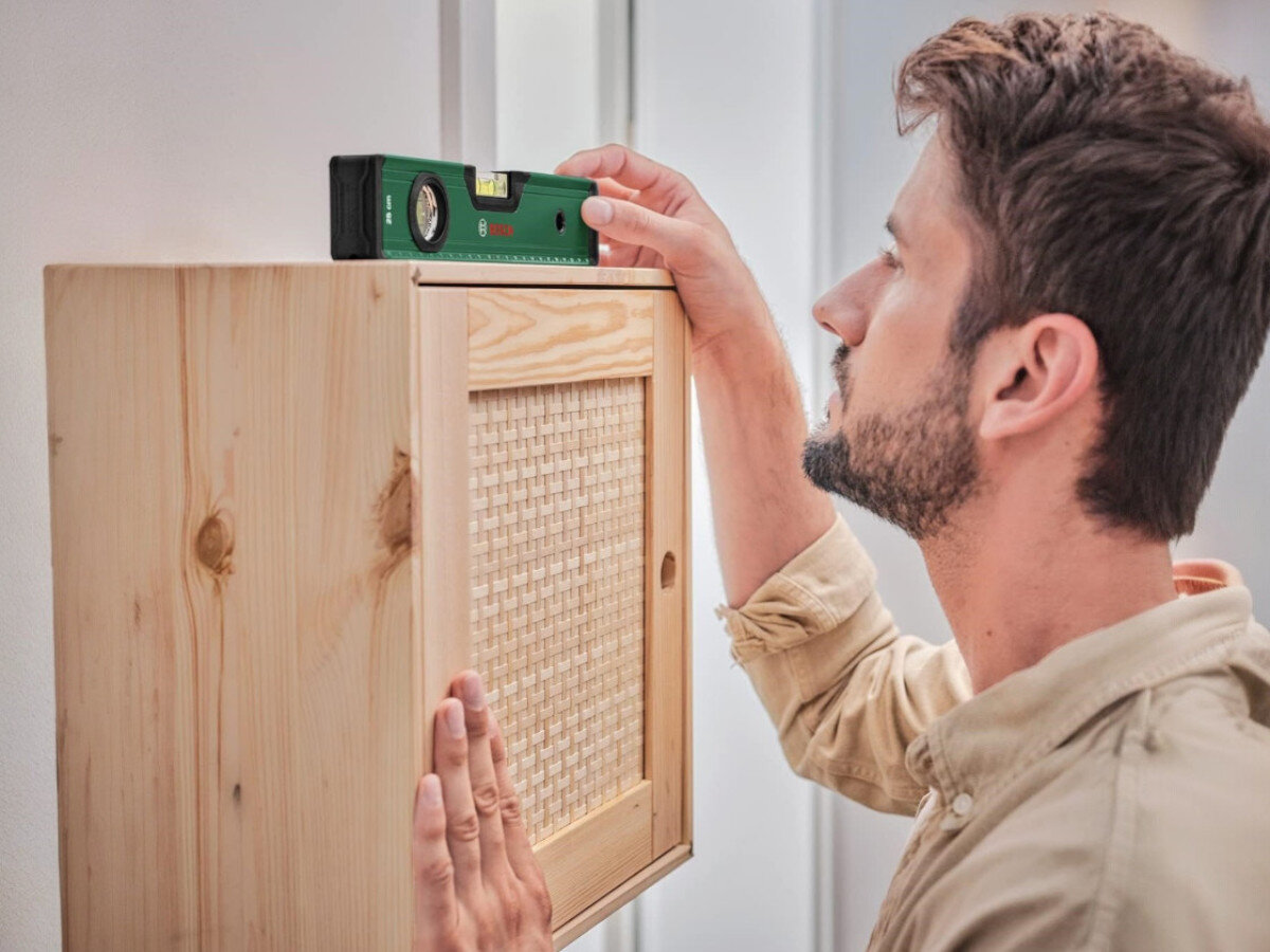 Poziomica BOSCH 1600A027PL, poziomica, pomiar, budowa, dokładność, mężczyzna odmierza poziom szafki ściennej