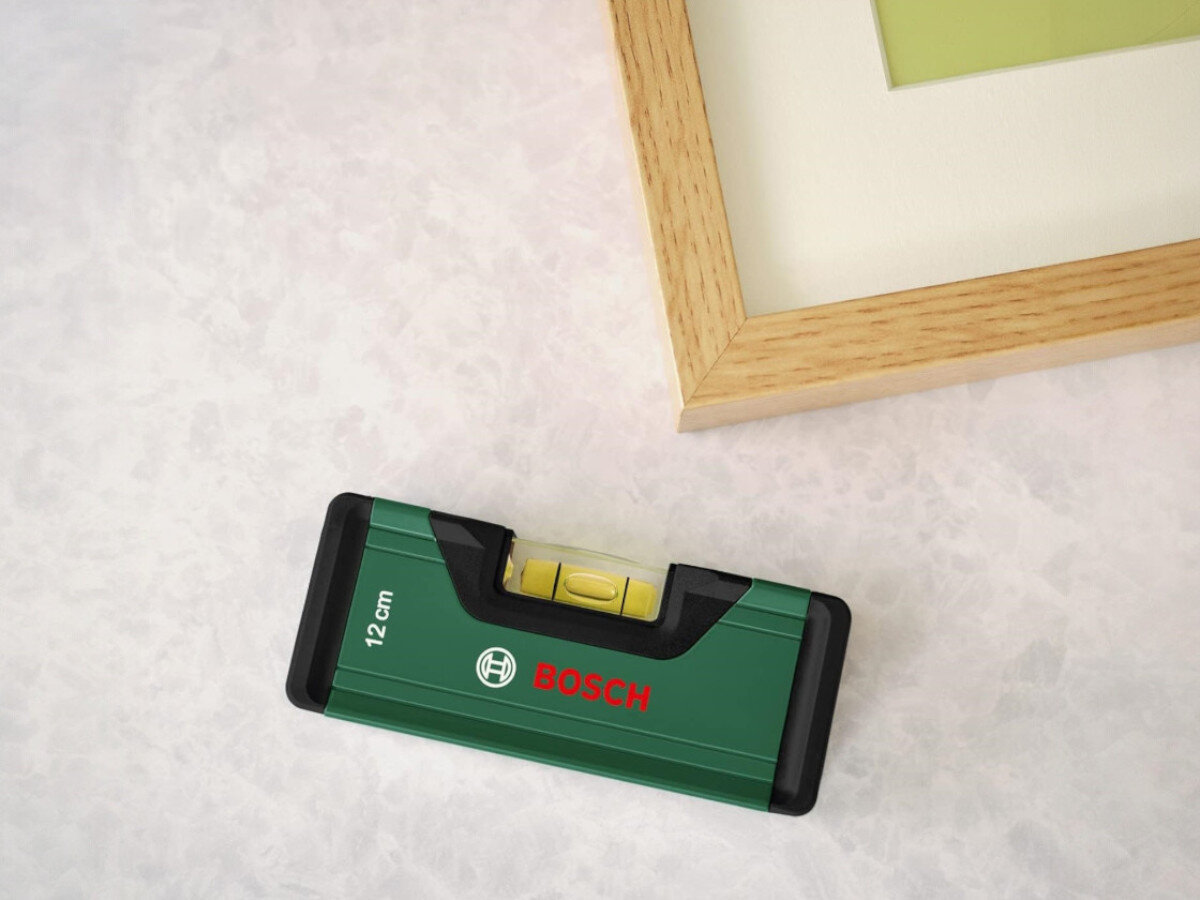 Poziomica BOSCH 1600A02H3H, libella, odczyt, fluorescencja, widoczność, Mała poziomica Bosch 12 cm leżąca na jasnym podłożu.