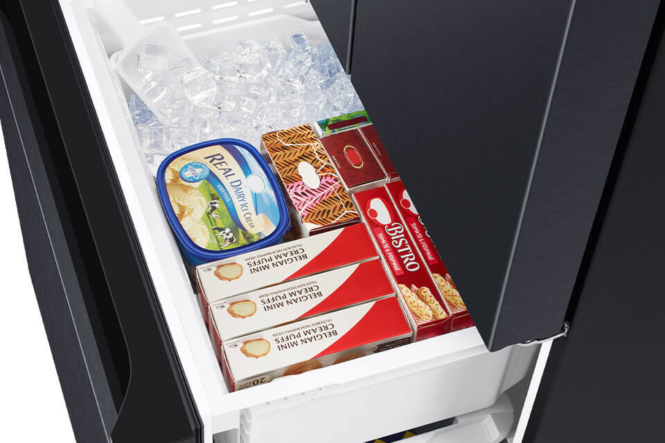 Wnętrze szuflady zamrażarki z kostkami lodu, pojemnikiem lodów \'REAL DAIRY ICE CREAM\' oraz opakowaniami lodów na patyku i wafelków \'BISTRO\'.