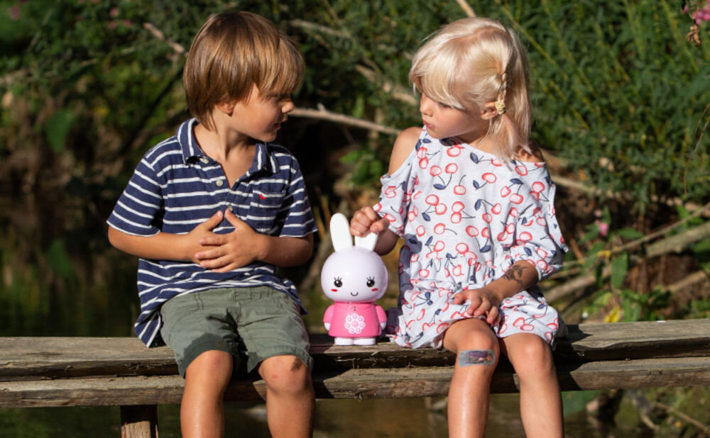Zabawka edukacyjna ALILO Honey Bunny G6 Różowy towarzysz Twojego dziecka, dzieci siedzące na ławce, produkt między nimi