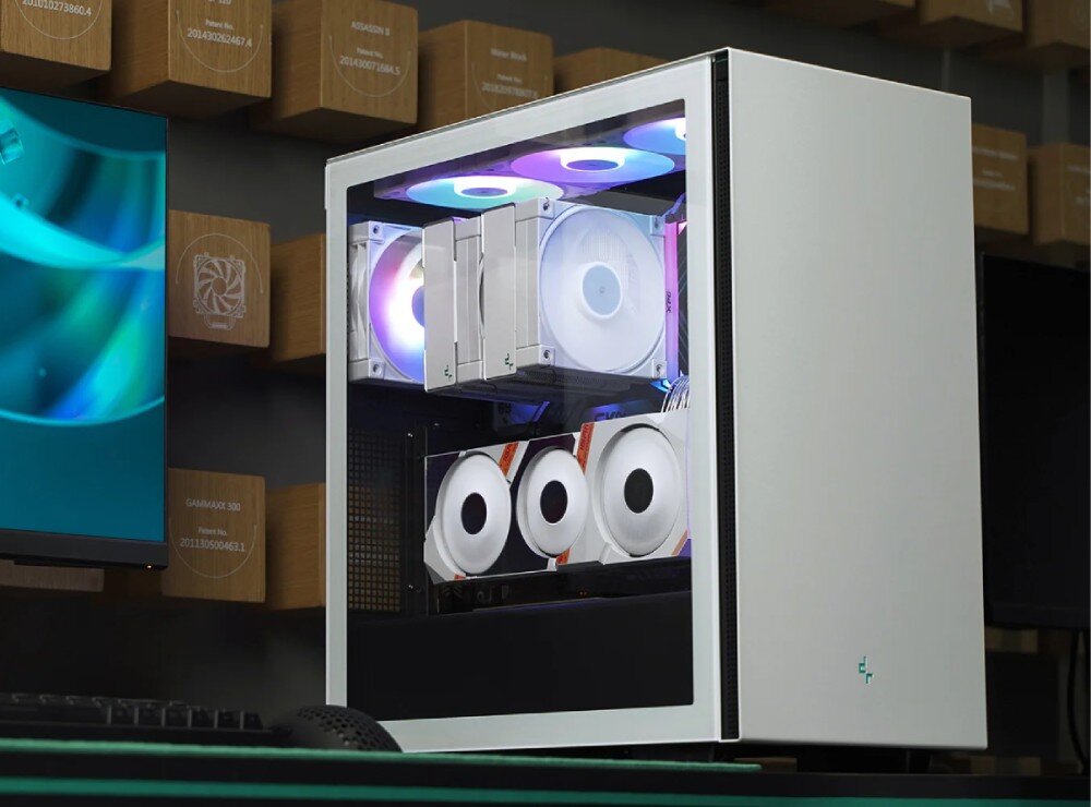 Obudowa DEEPCOOL CH510 Komputer stacjonarny w obudowie z przeszklonym bokiem stoi na biurku obok monitora i klawiatury. Wewnątrz widoczne są podzespoły z kolorowym podświetleniem, w tym karta graficzna zamontowana pionowo oraz chłodzenie wodne procesora