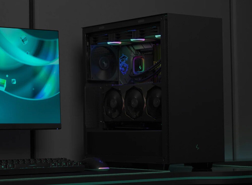 Obudowa DEEPCOOL CH510 Komputer stacjonarny w czarnej obudowie z przeszklonym bokiem stoi na biurku obok monitora i klawiatury. Wewnątrz widoczne są podzespoły z kolorowym podświetleniem, w tym karta graficzna zamontowana pionowo oraz chłodzenie wodne procesora