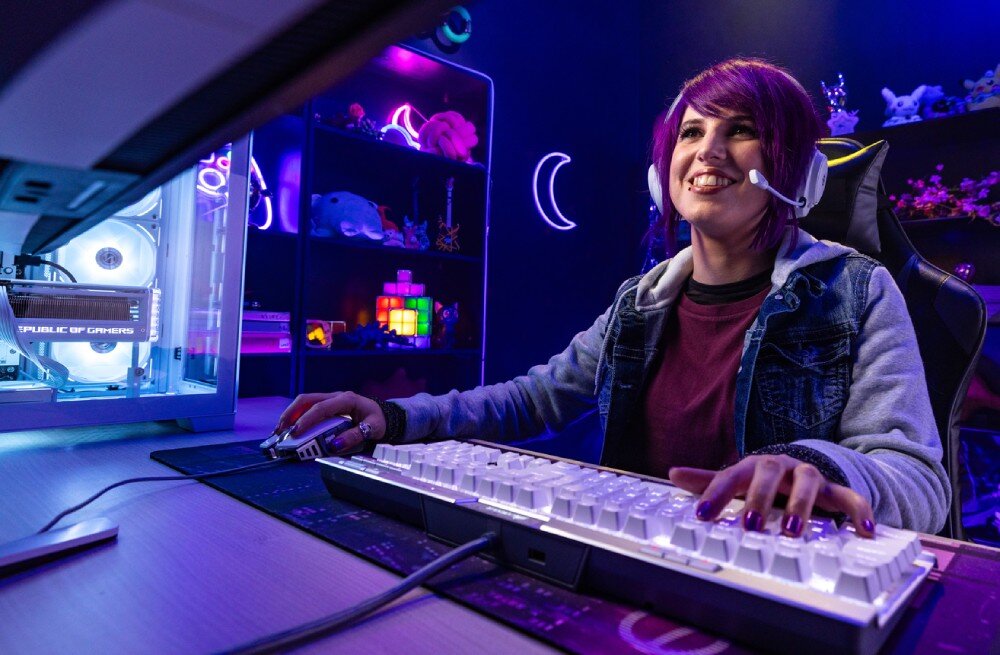 Pamięć RAM CRUCIAL Pro 32GB (2x16GB) 6000MHz Uśmiechnięta osoba z zestawem słuchawkowym grająca przy komputerze stacjonarnym z podświetloną obudową i akcesoriami w pokoju z fioletowym oświetleniem, parametry, taktowanie, opóźnienia, pojemność