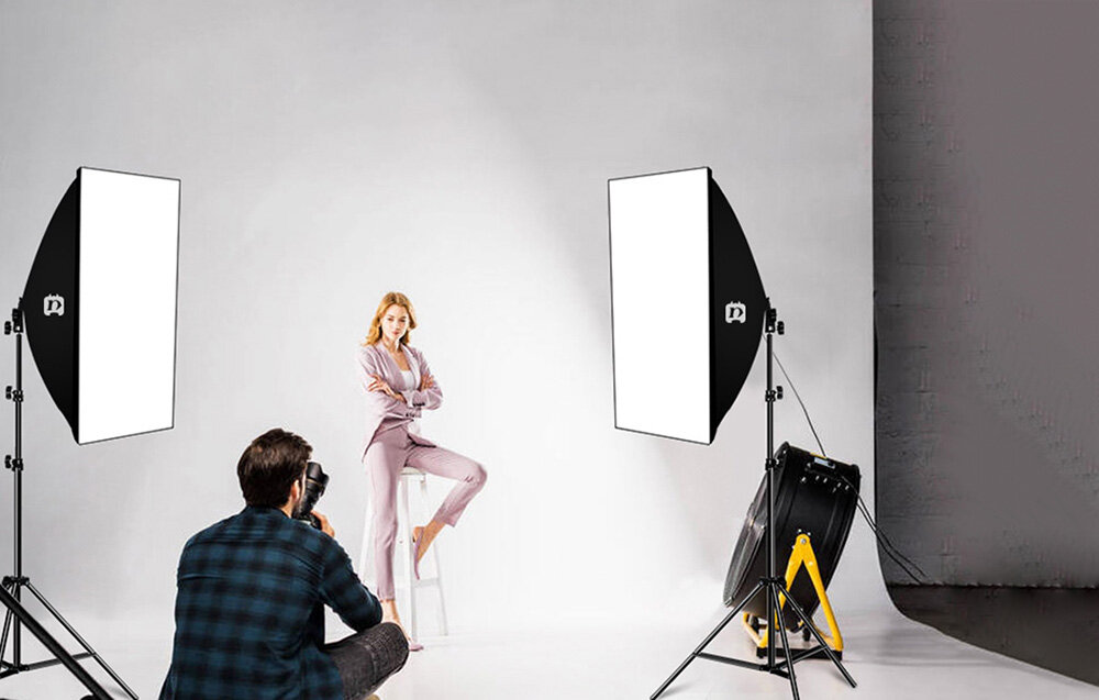 Fotograf wykonuje sesję zdjęciową modelki w studio z użyciem dwóch dużych softboxów ustawionych po bokach.