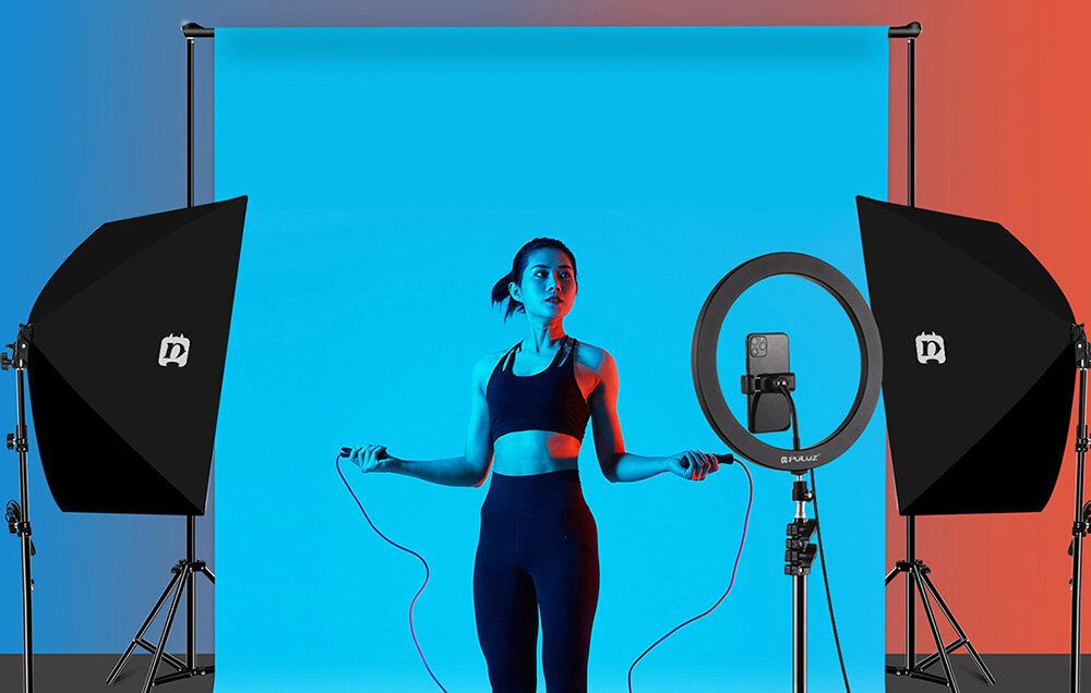 Studio fotograficzne z dwoma softboxami i lampą pierścieniową oświetlającymi modelkę na niebieskim tle.
