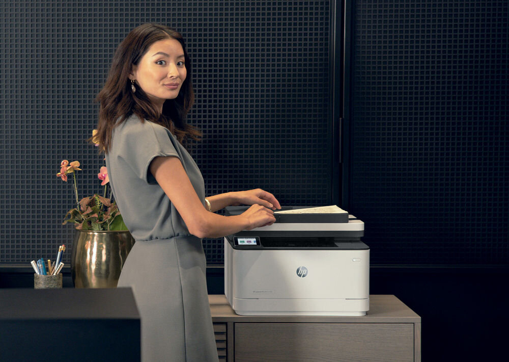 Urządzenie wielofunkcyjne HP LaserJet Pro 3102fdw Automatyczny druk dwustronny, Wi-Fi, Bluetooth kobieta stojąca przy urządzeniu ciemne tło Toner HP JetIntelligence ekologiczne i wydajne drukowanie