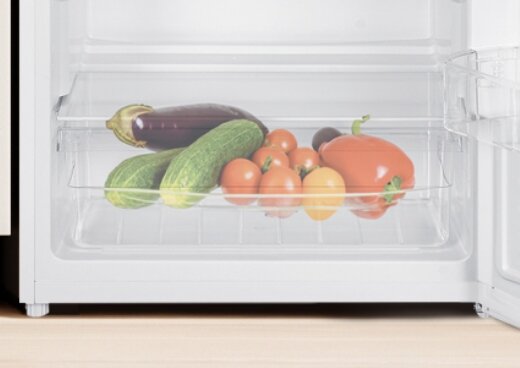Zbliżenie na wnętrze lodówki z przezroczystym pojemnikiem, w którym znajdują się warzywa.