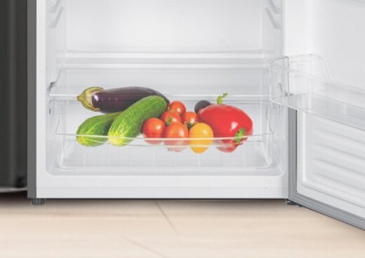 Zbliżenie na wnętrze lodówki z przezroczystym pojemnikiem, w którym znajdują się warzywa.
