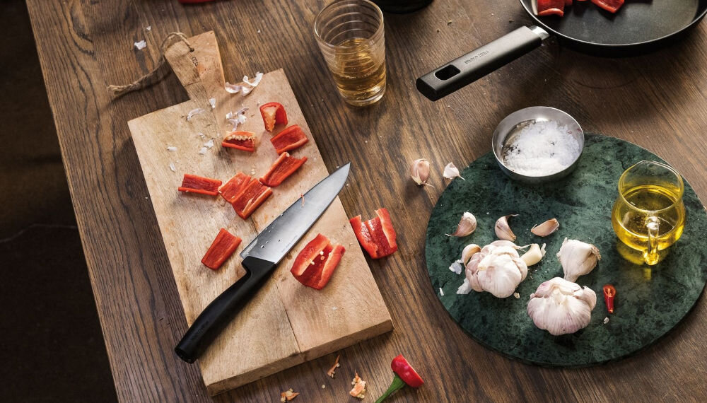 Nóż FISKARS Hard Edge 1051748 deska na desce znajduje się nóż z czarną rękojeścią obok leżą pokrojone warzywa dla każdego Ostrze o długości 17,2 cm całkowitej długości 30,1 cm krojenie szatkowanie porcjowanie waży jedynie 106 g