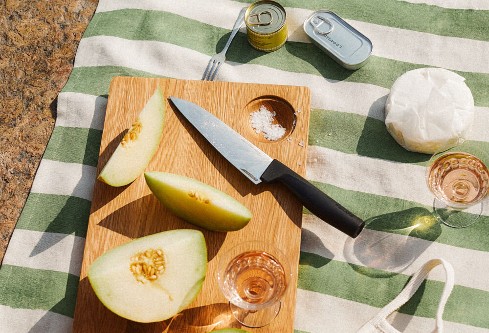 Nóż FISKARS Hard Edge 1051748 nóż z czarną rączką leży na desce obok rozkrojonych owoców  Ostrze z wysokiej jakości japońskiej stali nierdzewnej precyzja efektywność trwałość dynamiczne cięcie z dużą siłą subtelna precyzja w codziennym gotowaniu przy wymagających technikach kulinarnych