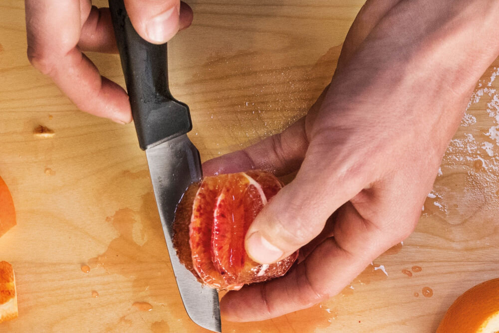 Nóż FISKARS Hard Edge 1051777 osoba kroi owoce na desce nożem z czarną rączką Ostrze z wysokiej jakości japońskiej stali nierdzewnej precyzja efektywność trwałość dynamiczne cięcie z dużą siłą subtelna precyzja w codziennym gotowaniu przy wymagających technikach kulinarnych