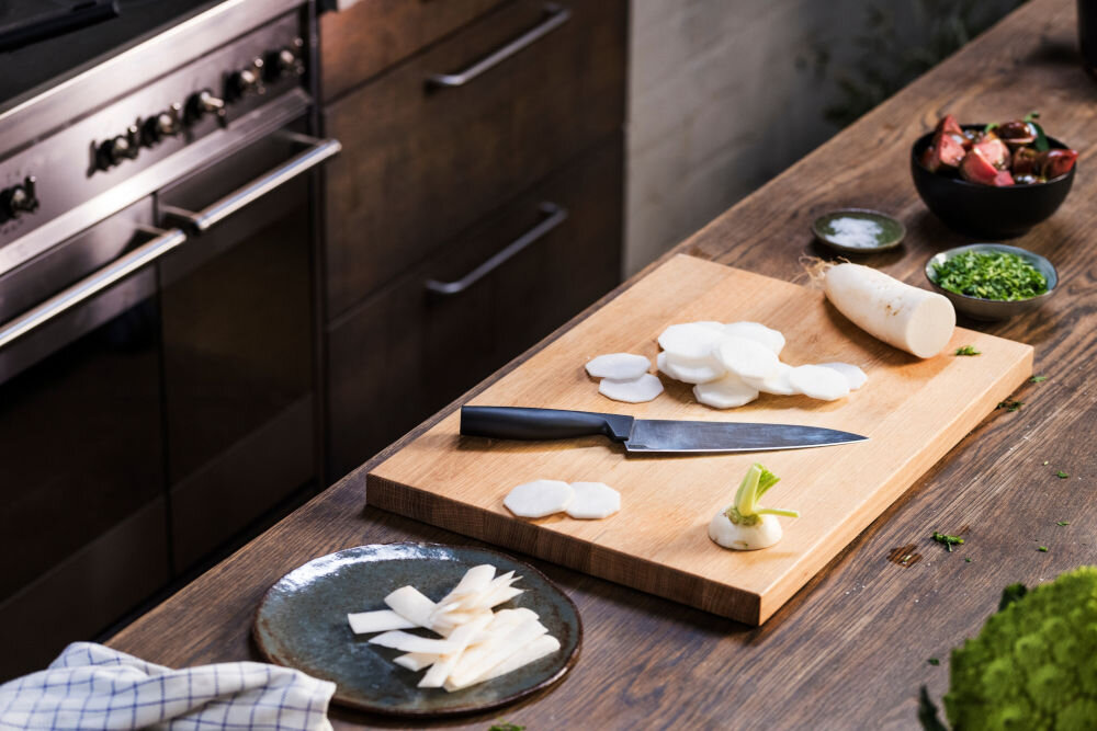 Nóż FISKARS Hard Edge 1051747 deska na desce znajduje się nóż z czarną rękojeścią obok leżą pokrojone warzywa dla każdego Ostrze o długości 20 cm całkowitej długośći 33,1 cm krojenie siekanie porcjowanie waży jedynie 120 g