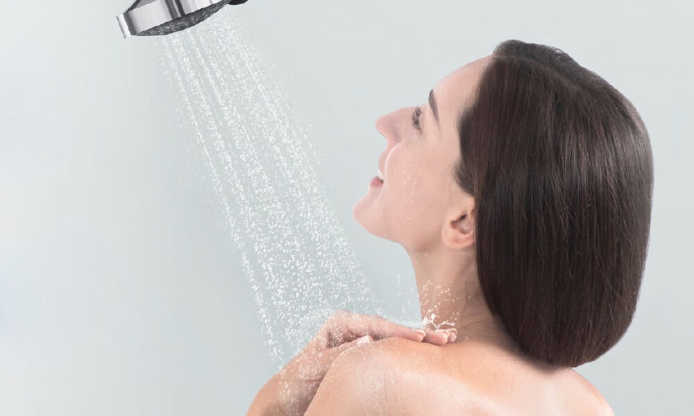 Filtr prysznicowy PHILIPS ASH138/10 Uśmiechnięta kobieta biorąca prysznic pod strumieniem wody z nowoczesnej słuchawki prysznicowej Philips.