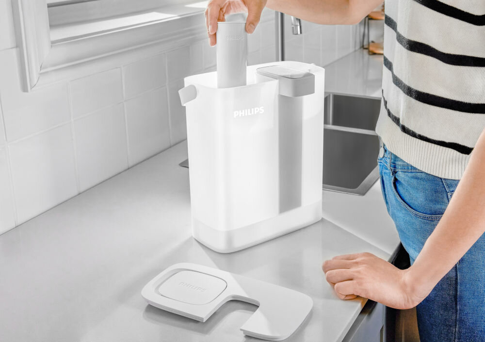 Dzbanek filtrujący PHILIPS AWP2980WH3/10 Biały dzbanek filtrujący Philips wyeksponowany na kuchennym stole w otoczeniu świeżych warzyw i ziół. Zdjęcie podkreśla dużą pojemność urządzenia, idealną do przygotowywania zdrowych posiłków i napojów dla całej rodziny.