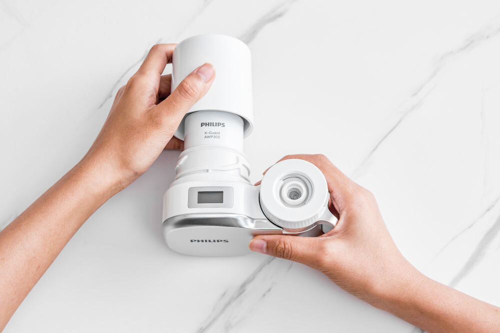 Filtr na kran PHILIPS AWP3705P1/10 X-Guard Zbliżenie na dłonie montujące biały wkład filtrujący Philips X-Guard AWP305 do obudowy filtra nakranowego
