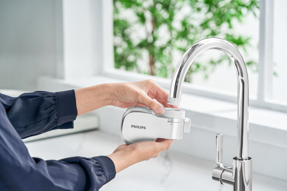 Filtr na kran PHILIPS AWP3705P1/10 Osoba montująca biały filtr nakranowy Philips na srebrnej wylewce baterii kuchennej.