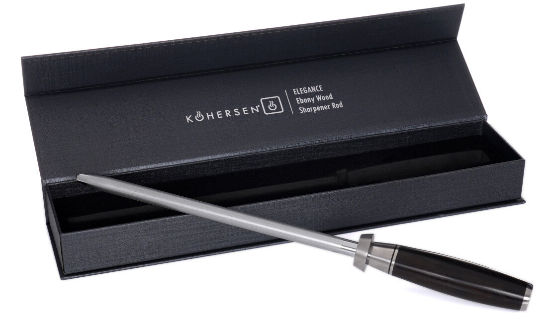 Na obrazie widoczna jest ostrzałka z metalowym prętem i ciemną rączką, umieszczona na otwartym pudełku. Na pudełku znajduje się napis: \'KOHERSEN Elegance Ebony Wood Sharpener Rod\'.