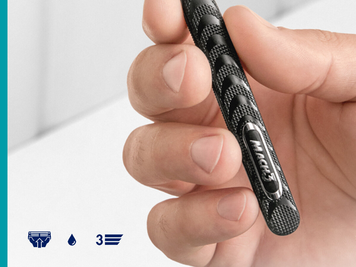 Golarka GILLETTE Mach3 + 5 ostrzy Zbliżenie na dłoń trzymającą czarną, teksturowaną rączkę maszynki do golenia Gillette Mach3. U dołu ikonki maszynki, kropli i cyfry 3.