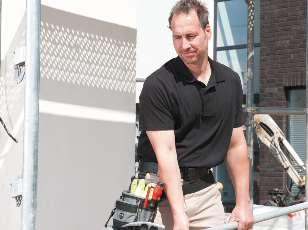 Torba narzędziowa EINHELL 49907710 plac budowy osoba podnosi metalową rurkę do pasa ma przytwierdzoną torbę organizacja pracy praktyczność uniwersalne zastosowanie