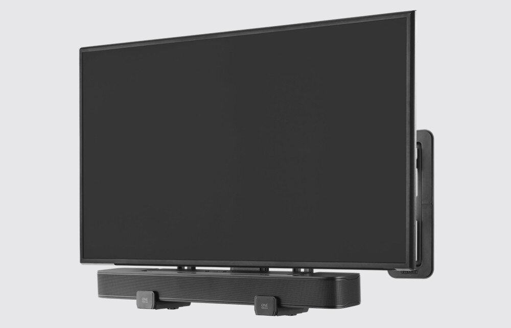 Na obrazie widoczny jest telewizor zamontowany na ścianie, poniżej którego znajduje się soundbar przymocowany uchwytem. Na uchwycie widoczny jest napis \'ONE FOR ALL\'.