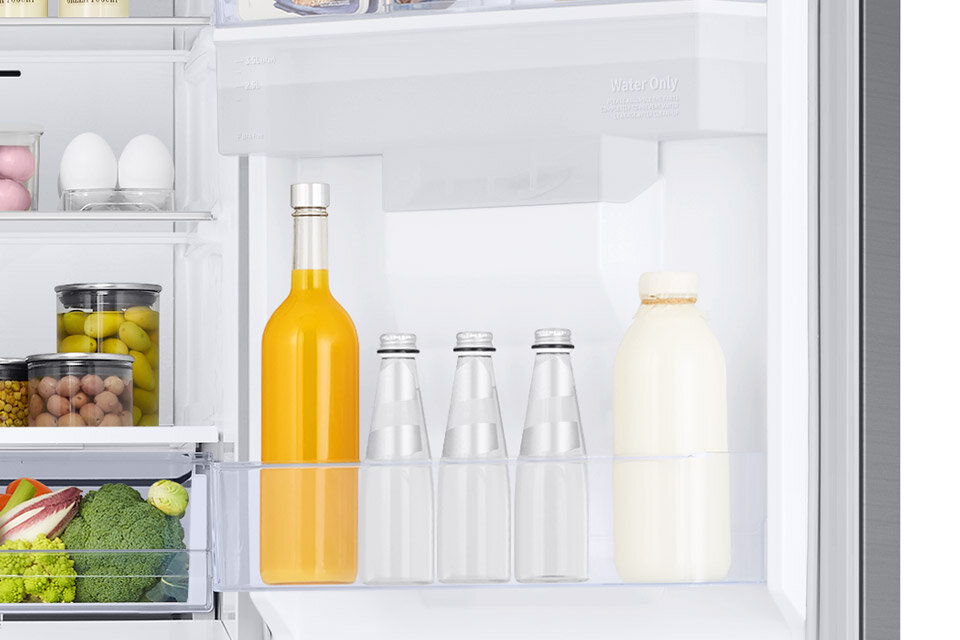 Wnętrze lodówki z widocznymi półkami, na których znajdują się butelki z napojami, słoiki z przetworami oraz jajka. Na drzwiach lodówki widoczny jest napis \'Water Only\'.