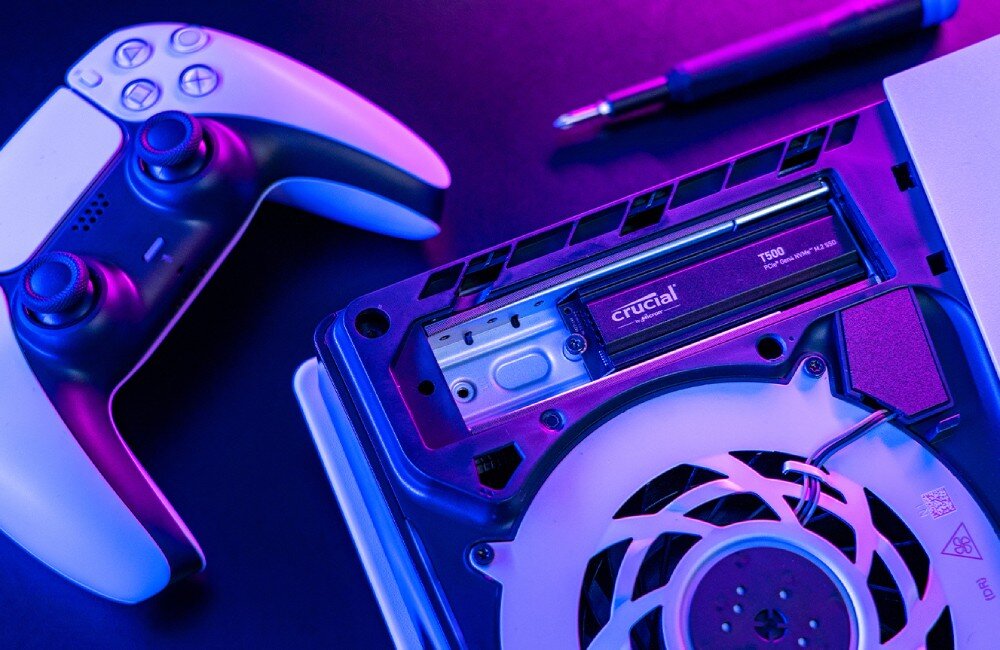 Dysk CRUCIAL T500 Czarny dysk SSD zamontowany wewnątrz konsoli do gier, widoczny wentylator, pad i śrubokręt w tle, radiator, kompatybilność z PS5