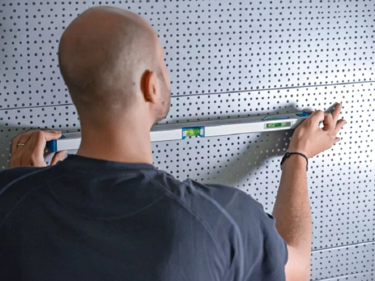 Poziomnica ręczna BOSCH 1600A01V3Y, poziomica, pomiar, pion, poziom , osoba odmierza poziom ściany perforowanej