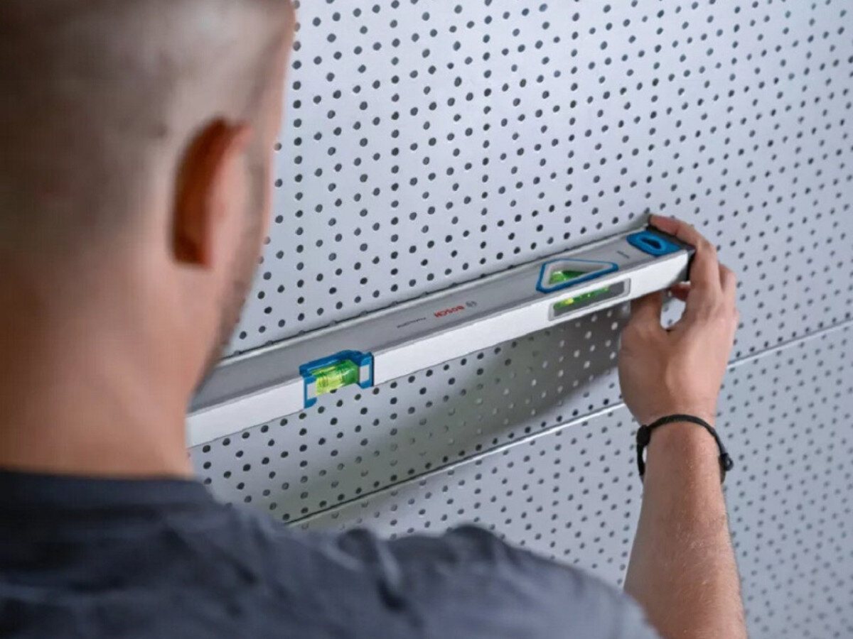 Poziomnica ręczna BOSCH 1600A01V3Y, guma, stabilność, ochrona, waga, osoba przymierza poziomice poziomo do perforowanej ściany