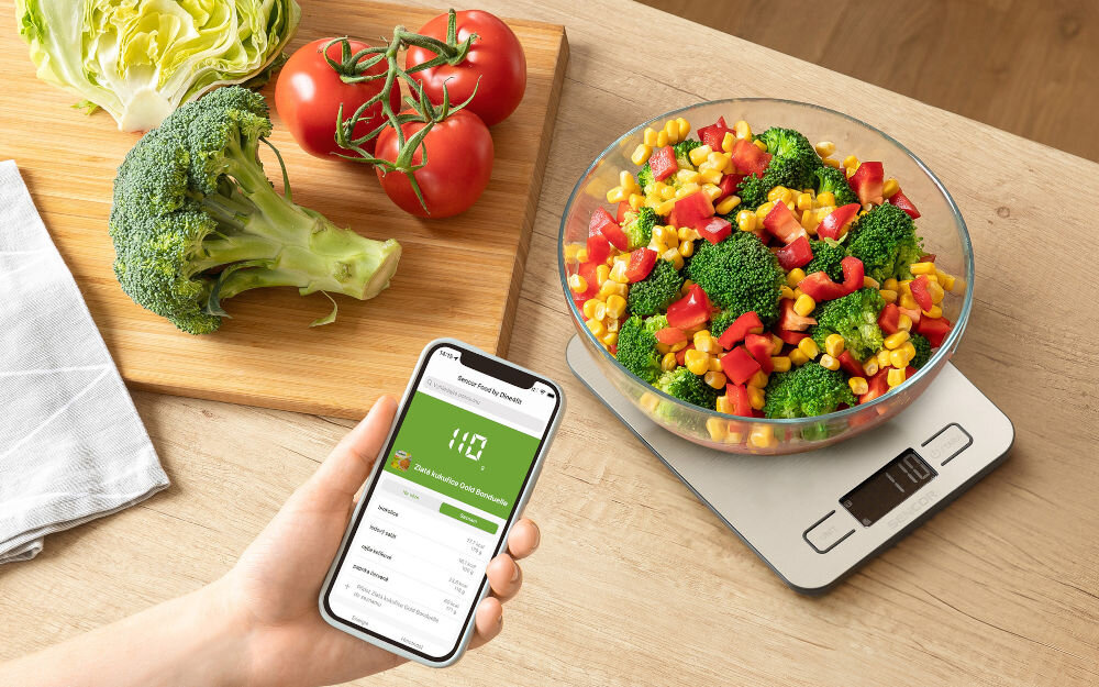 Waga kuchenna SENCOR SKS 8080 Srebrny srebrna waga przyciski wyświetlacz na wadze miska z warzywami osoba trzyma telefon z aplikacją Aplikacja SENCOR FOOD (Android i iOS) z twórcami aplikacji Dine4Fit funkcjonalność intuicyjny interfejs obszerna regularnie aktualizowana baza danych online dostęp do ponad 400 000 produktów spożywczych łatwe skanowanie kodów EAN 