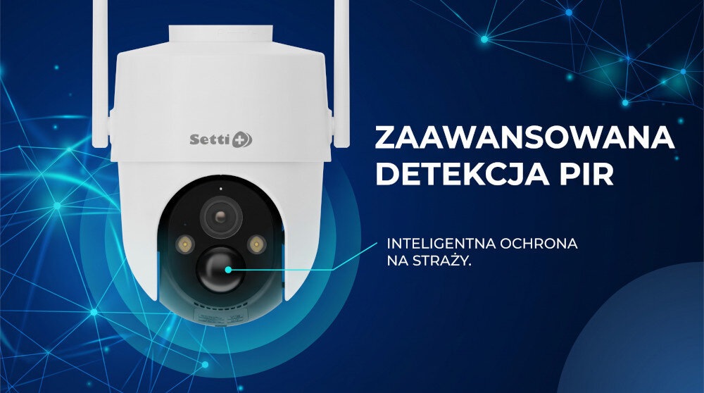 Na tarasie przy domu znajduje się drewniany leżak z niebieskim materacem. W tle widać stos drewna oraz roślinność, a na ścianie zamontowana jest kamera i panel słoneczny.