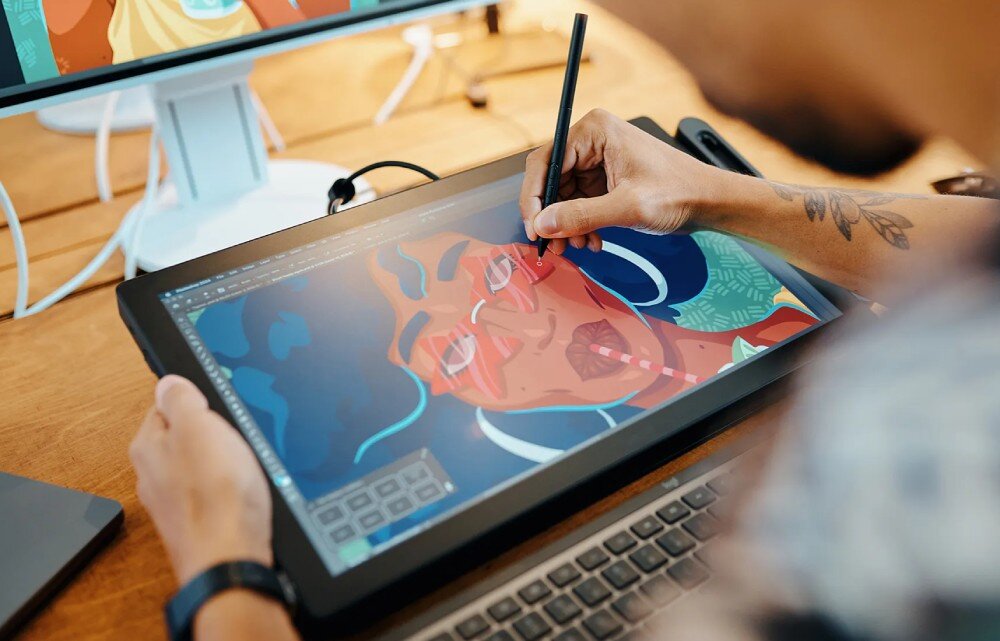 Tablet graficzny WACOM Cintiq Pro 17 Osoba trzyma tablet graficzny i rysuje na nim postać z wielkimi słuchawkami, używając rysika. Na ekranie widoczna jest kolorowa grafika z wizerunkiem osoby w słuchawkach, opis