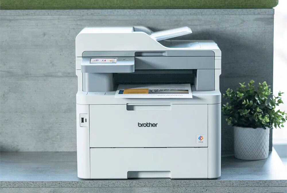 Urządzenie wielofunkcyjne BROTHER MFC-L8340CDW Druk w kolorze, Automatyczny druk dwustronny, Wi-Fi prezentacja urządzenia na półce obok roślina w doniczce
