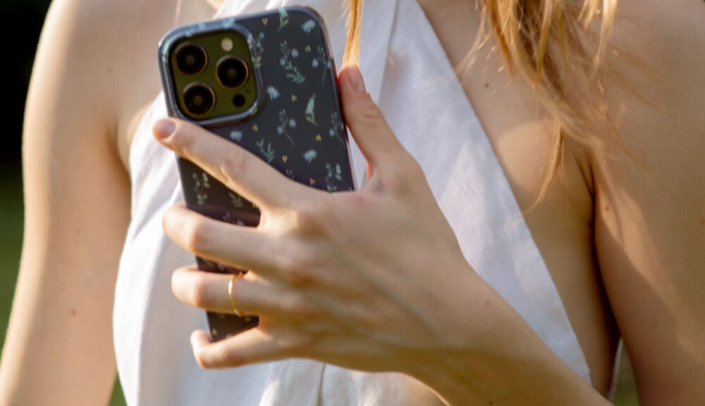 Osoba trzyma telefon w granatowym etui z delikatnym wzorem roślinnym. Etui ma wycięcia na aparat i przyciski.