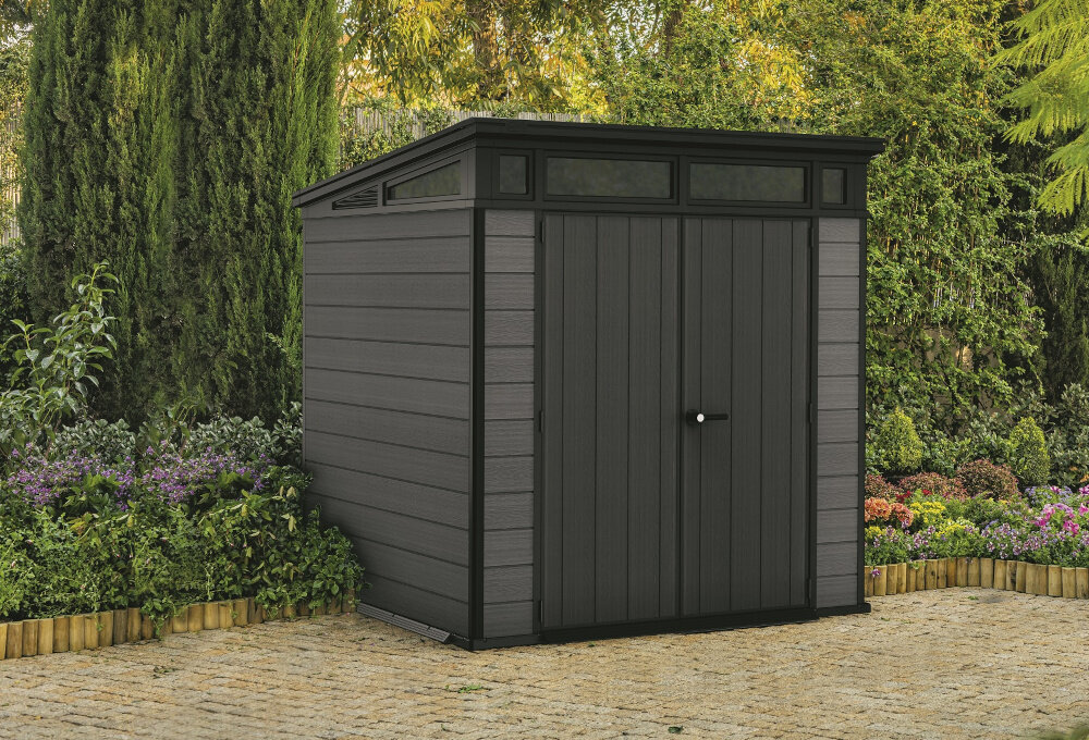 Domek narzędziowy KETER Cortina 7X7 255044 Szary domek na ziemi w tle drzewa i rośliny z wysokiej jakoś tworzywa kompozytowego EVOTECH+ o grubości 20 mm duża wytrzymałość odporny na działanie wilgoci promieni UV i zmiany temperatur około 15% materiałów z recyklingu