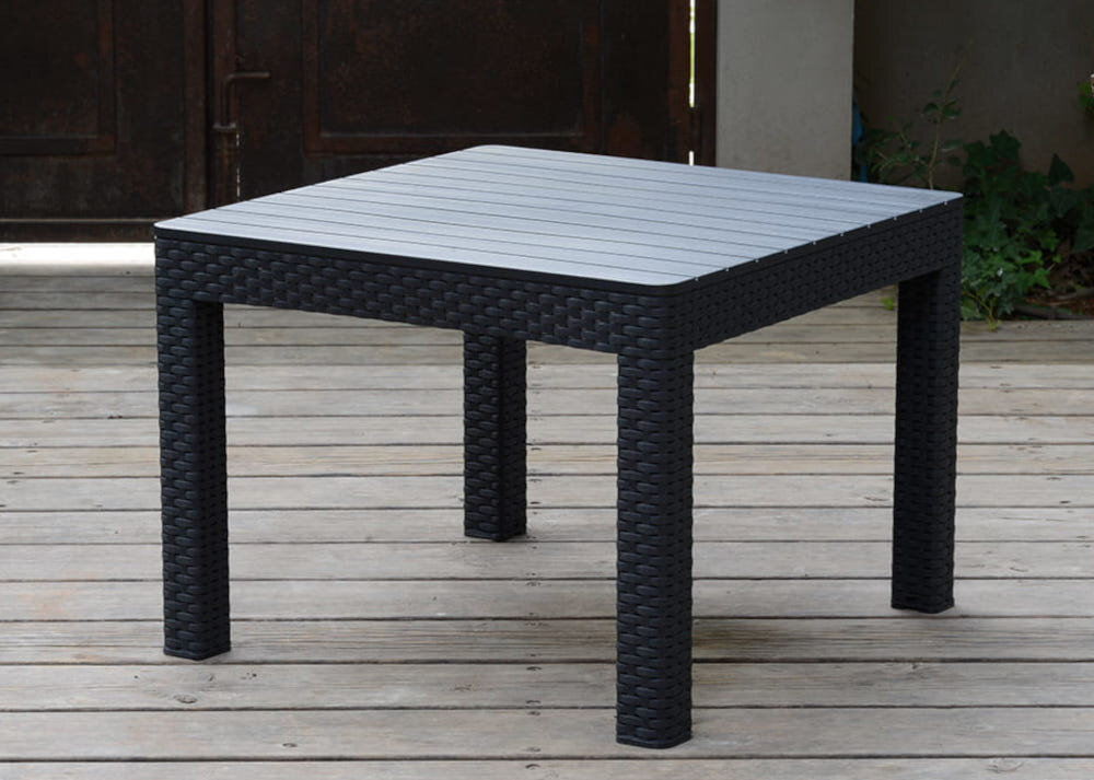 Zestaw mebli ogrodowych KETER Marie Corner 5 252710 Grafitowy stolik na drewnianej podłodze w tle drzwi i roślinka stolik kawowy o wymiarach 58.5 x 58.5 x 43 cm blat odporny na zarysowania wysoką temperaturę i wilgoć gładka powierzchnia ułatwia czyszczenie