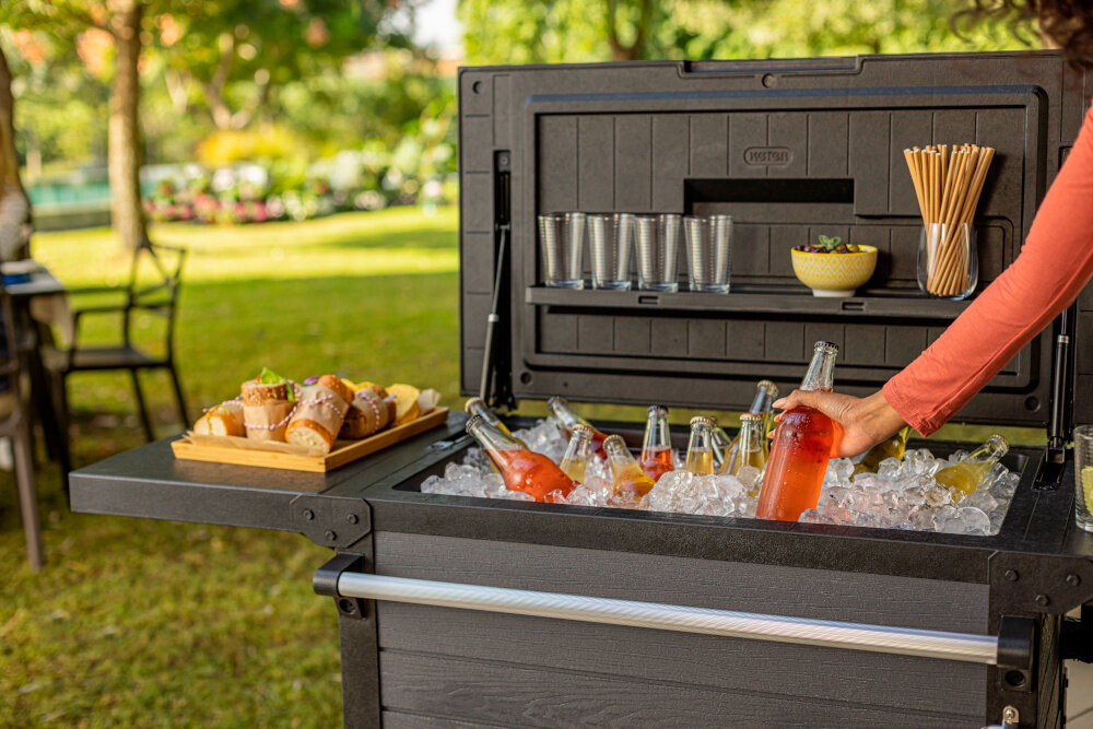 Barek ogrodowy KETER PATIO COOLER & BEVERAGE 255187 zbliżenie na wnętrze barku barek wypełniony kostkami lodu i butelkami przekąski szklanki klapa dodatkowy stolik udźwig do 50 kg praktyczny schowek na zimne napoje siłowniki płynne i kontrolowane otwieranie i zamykanie bezpieczeństwo użytkowania