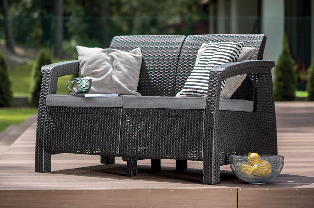Sofa ogrodowa KETER Corfu II Love 258973 Grafit sofa na tarasie w tle rośliny i dom sofa na tarasie obok latarnia w tle rośliny i drzewa odpoczynek na świeżym powietrzu miłe chwile w gronie rodzinnym lub z przyjaciółmi komfort relaks