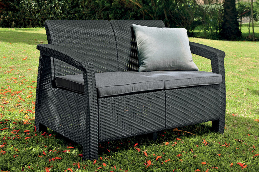 Sofa ogrodowa KETER Corfu II Love 258973 Grafit sofa na trawie w tle rośliny niewielkie rozmiary 28 x 70 x 79 cm odpoczynek na świeżym powietrzu obciążenie do 220 kg