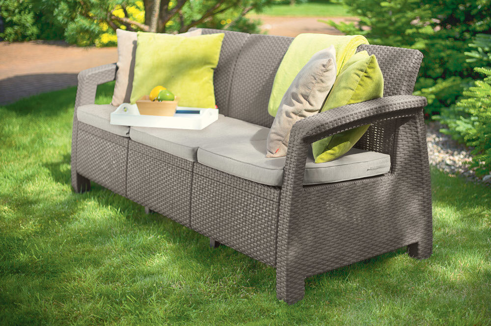 Sofa ogrodowa KETER Corfu II Max Love - OAT 258978 Cappuccino sofa na trawie w tle drzewa i rośliny trzy wygodne poduszki komfortowy odpoczynek łatwe utrzymanie czystości