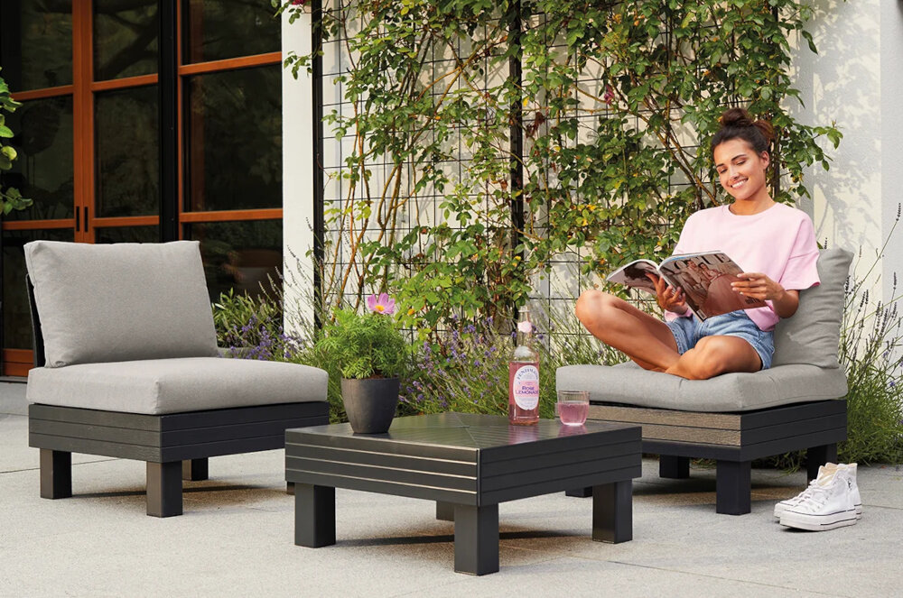 Zestaw mebli ogrodowych KETER 1 Elements 257366 Grafitowy zestaw na tarasie siedziska ustawione obok siebie w tle dom i rośliny z wysokiej jakości tworzywa sztucznego i polipropylenu odporność na zmienne warunki atmosferyczne nie blaknie pod wpływem słońca nie odkształca się od wilgoci