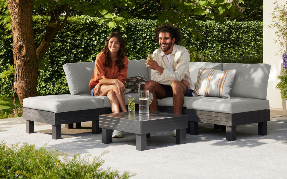 Zestaw mebli ogrodowych KETER Elements Single Hocker 257368 Grafitowy dwie osoby siedzą na sofie ogrodowej w tle dom i rośliny z wysokiej jakości tworzywa sztucznego i polipropylenu odporność na zmienne warunki atmosferyczne nie blaknie pod wpływem słońca nie odkształca się od wilgoci