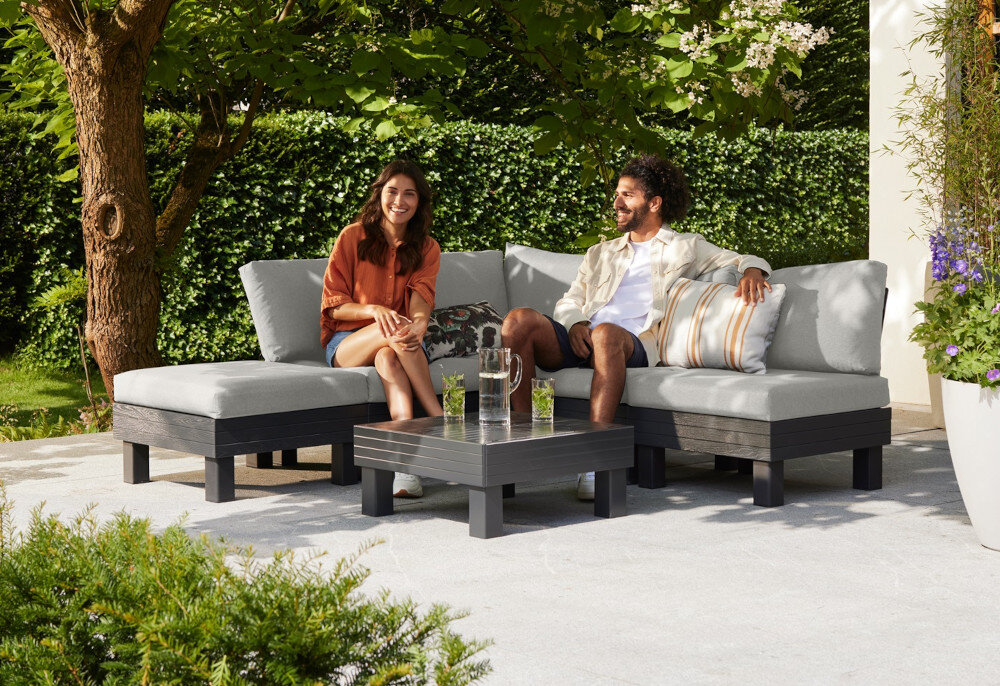 Zestaw mebli ogrodowych KETER Elements Single Hocker 257368 Grafitowy dwie osoby siedzą na sofie ogrodowej w tle dom i rośliny odporność na zabrudzenia łatwe do wyczyszczenia oszczędność czasu i wysiłku oszczędność ekologia