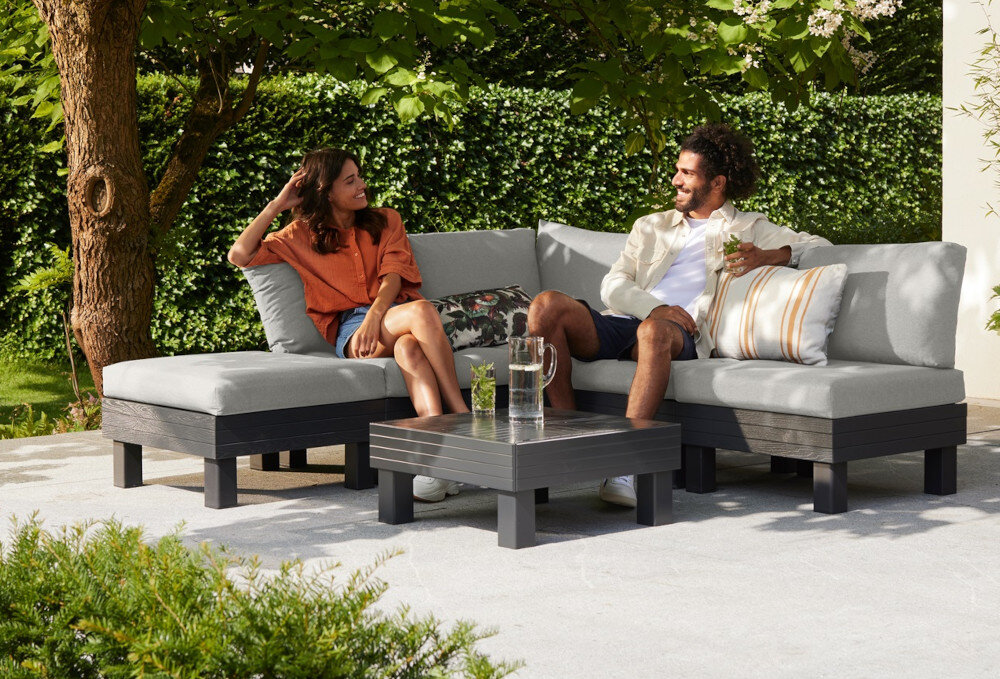 Zestaw mebli ogrodowych KETER Elements Single Hocker 257368 Grafitowy taras dwie osoby każda siedzi na osobnym module w tle żywopłot dom i rośliny grafitowy stelaż jasnoszare poduszki elegancka neutralna kompozycja kolorystyczna dopasujesz do różnych stylów aranżacyjnych zestaw nie jest składany odporność na pogodę na zewnątrz przez cały sezon nie wymaga konserwacji ani zabezpieczenia