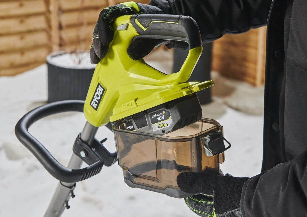 Odśnieżarka akumulatorowa RYOBI RY18ST25A-140 podwórko osoba trzyma odśnieżarkę w dłoniach zakłada osłonę na akumulator akumulator o pojemności 4,0Ah z serii ONE+ umożliwia odśnieżenie powierzchni do 100 m² na jednym ładowani można sprawnie oczyścić całą posesję za jednym razem brak kabli oraz paliwa zwiększa swobodę ruchu ładowarka
