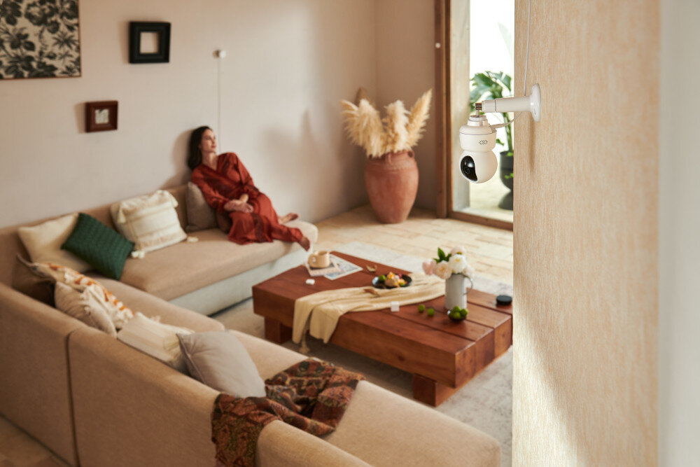 Kamera AQARA E1 CH-C01E - Dopasowane ustawienia, kamera przymocowana do ściany pomieszczenia, kobieta siedząca na kanapie